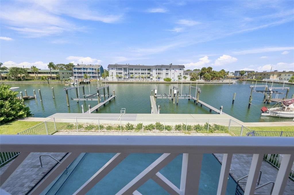 A balcony view overlooking a swimming pool, a boat dock, and a canal with buildings — 11797 1ST STREET E, TREASURE ISLAND, FL