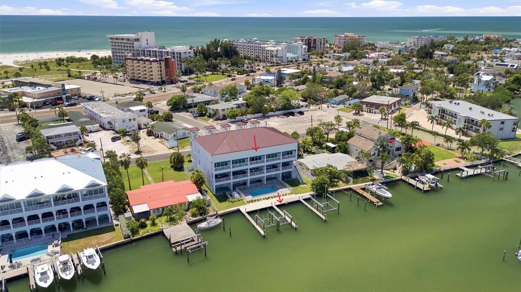 An aerial view shows a waterfront condominium building with a pool and private boat docks — 11797 1ST STREET E, TREASURE ISLAND, FL
