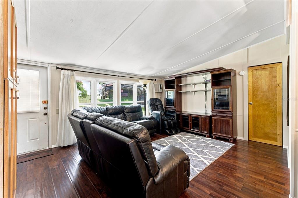 A living room features dark wood flooring, a black leather sectional, and a large entertainment center — 7608 W OTTER STREET, HOMOSASSA, FL