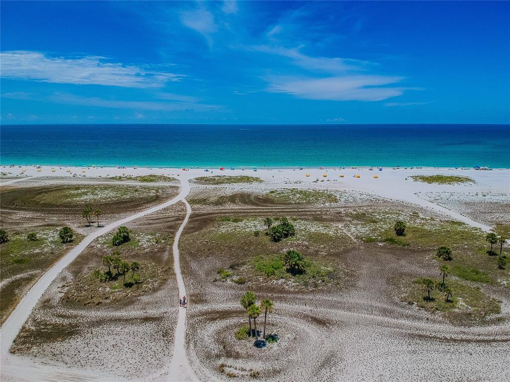 An aerial view of a white sand beach with umbrellas and the ocean beyond — 11605 GULF BOULEVARD UNIT 402, TREASURE ISLAND, FL