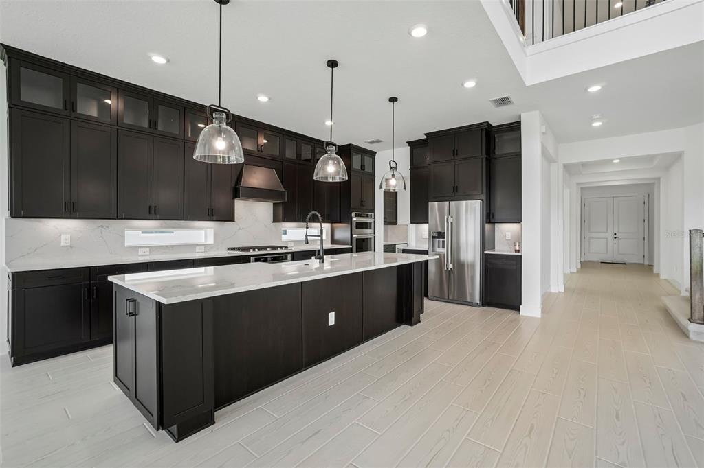 A modern kitchen features dark cabinetry, a large white quartz island, and light wood flooring — 34960 BLAINE PASS, ZEPHYRHILLS, FL