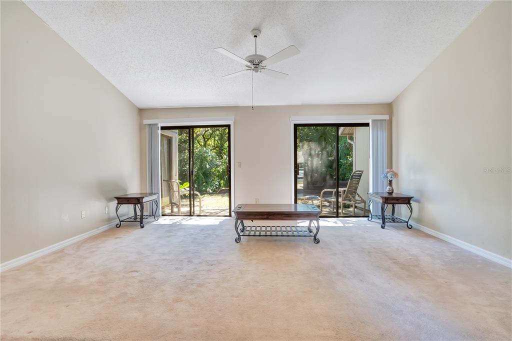 A living room features beige carpet, a vaulted ceiling, a ceiling fan, and two sliding doors — 4340 SEA MIST DRIVE, NEW SMYRNA BEACH, FL
