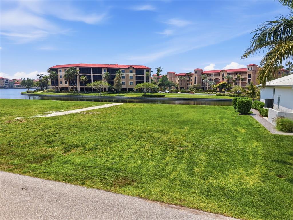 A grassy lawn overlooks a narrow canal with large multi-story apartment buildings in the background — 81 COLONY POINT DRIVE, PUNTA GORDA, FL