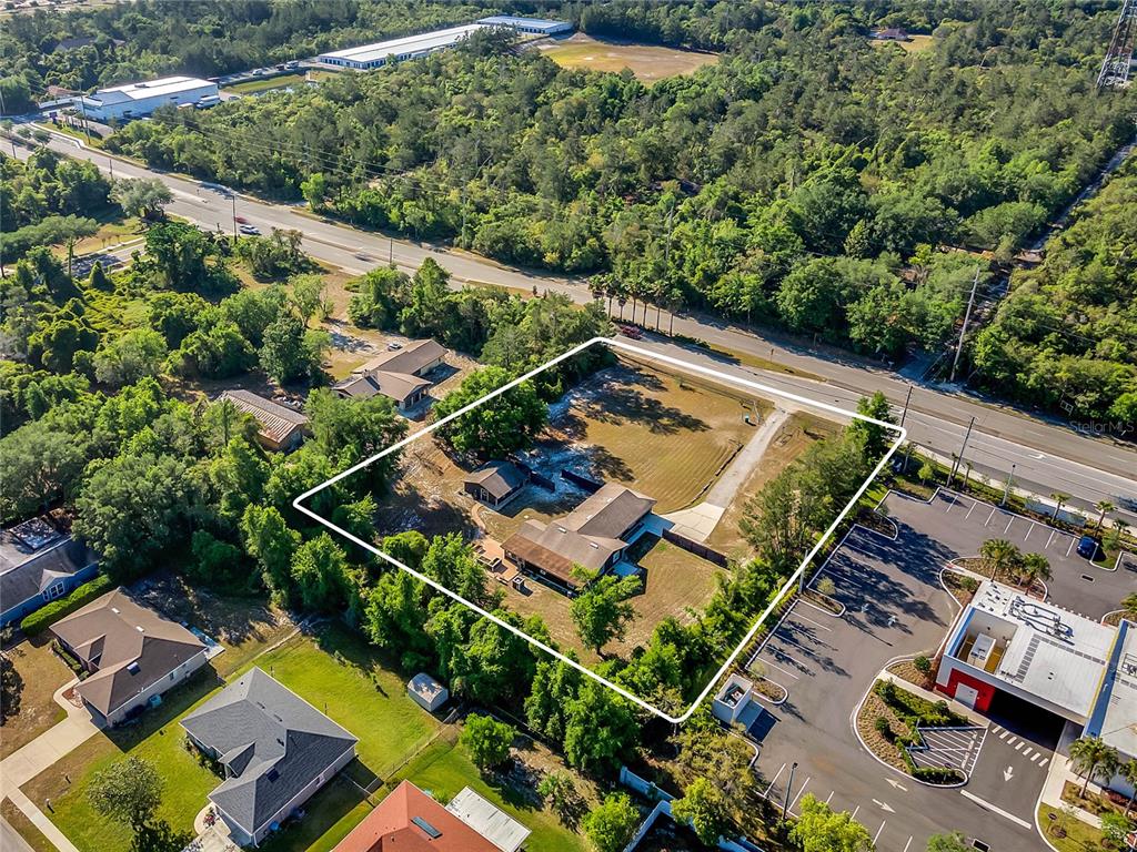 An aerial view shows a residential property outlined in white next to a commercial parking lot — 3086 HOWLAND BOULEVARD, DELTONA, FL