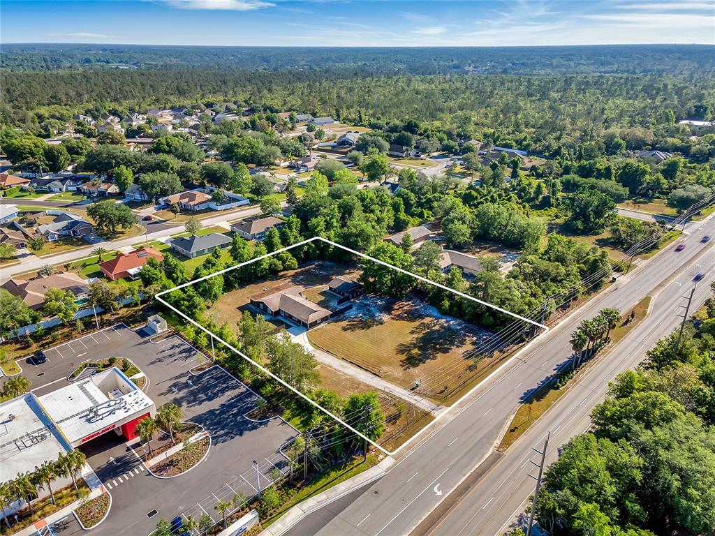 An aerial view shows a residential lot outlined in white next to a commercial building — 3086 HOWLAND BOULEVARD, DELTONA, FL