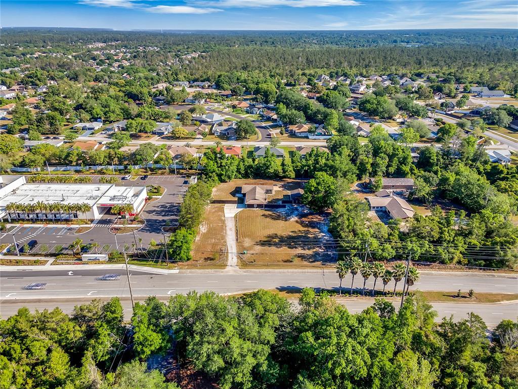 An aerial view shows a residential property with a long driveway situated near a commercial building — 3086 HOWLAND BOULEVARD, DELTONA, FL