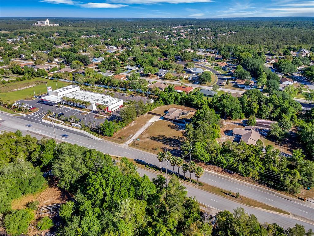 An aerial view shows a commercial building, residential homes, and a road surrounded by trees — 3086 HOWLAND BOULEVARD, DELTONA, FL