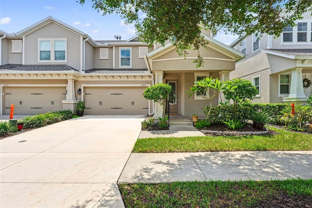 A two-story townhouse with a beige stucco exterior, two garage doors, and a front porch — 14507 ROCKY BROOK DRIVE, TAMPA, FL
