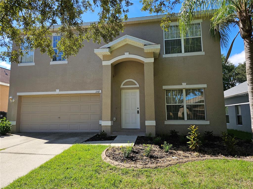 A two-story tan stucco house with a two-car garage and a covered front entryway — 1147 EMERALD HILL WAY, VALRICO, FL