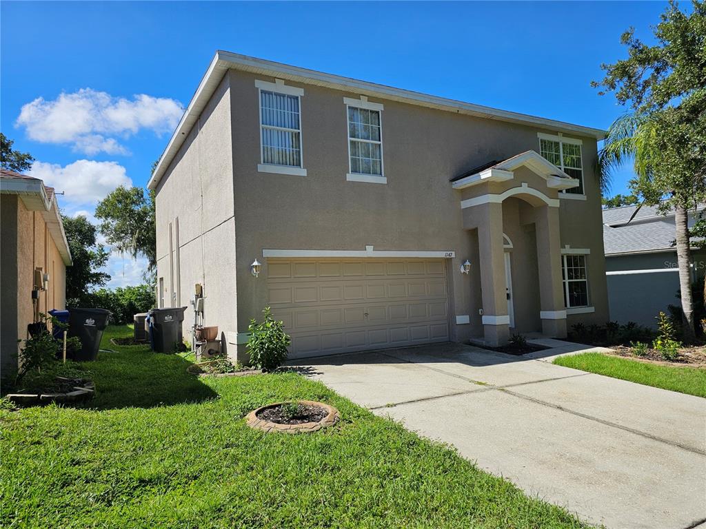 A two-story tan stucco house features a two-car garage and a concrete driveway — 1147 EMERALD HILL WAY, VALRICO, FL