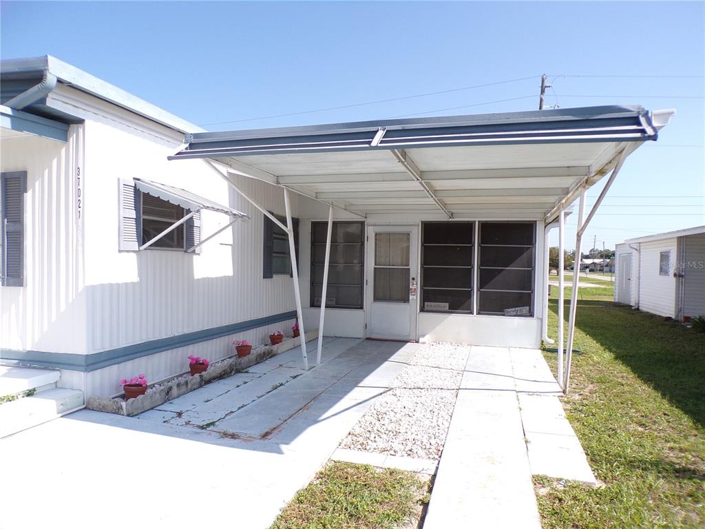 A white mobile home features a metal carport, a small front porch, and potted flowers — 37021 SANDRA AVENUE, ZEPHYRHILLS, FL