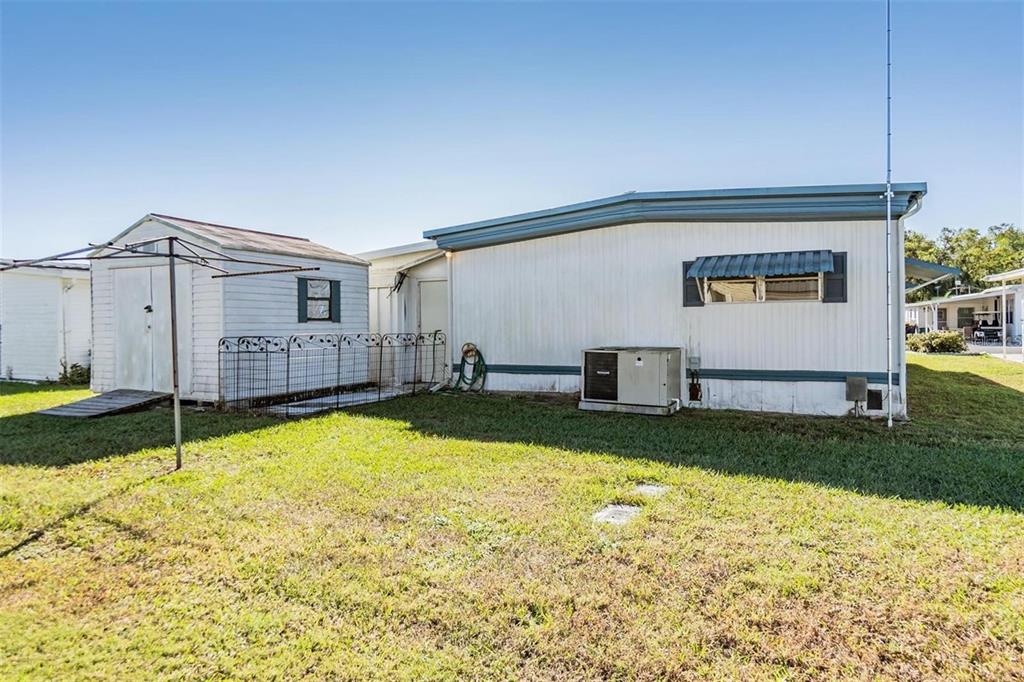 The exterior of a manufactured home features white siding, a storage shed, and a lawn — 37021 SANDRA AVENUE, ZEPHYRHILLS, FL