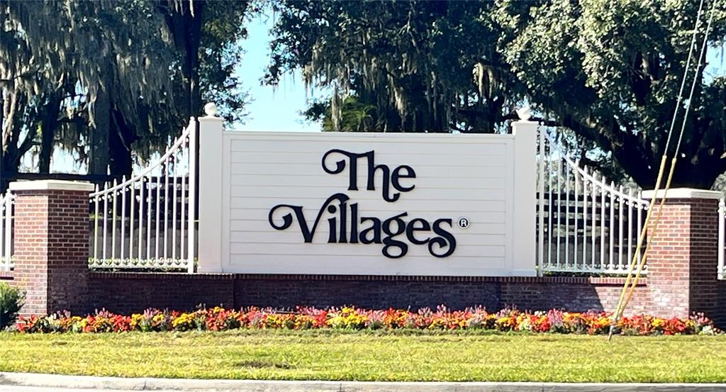 A white sign with the words The Villages stands behind a bed of colorful flowers — 9307 SE 159TH LANE, SUMMERFIELD, FL