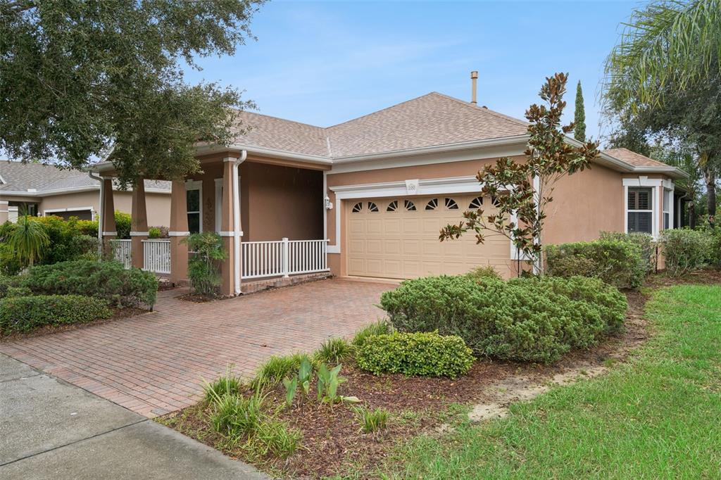 A single-story house with a tan stucco exterior, a brick driveway, and a front porch — 100 FLAME VINE WAY, GROVELAND, FL