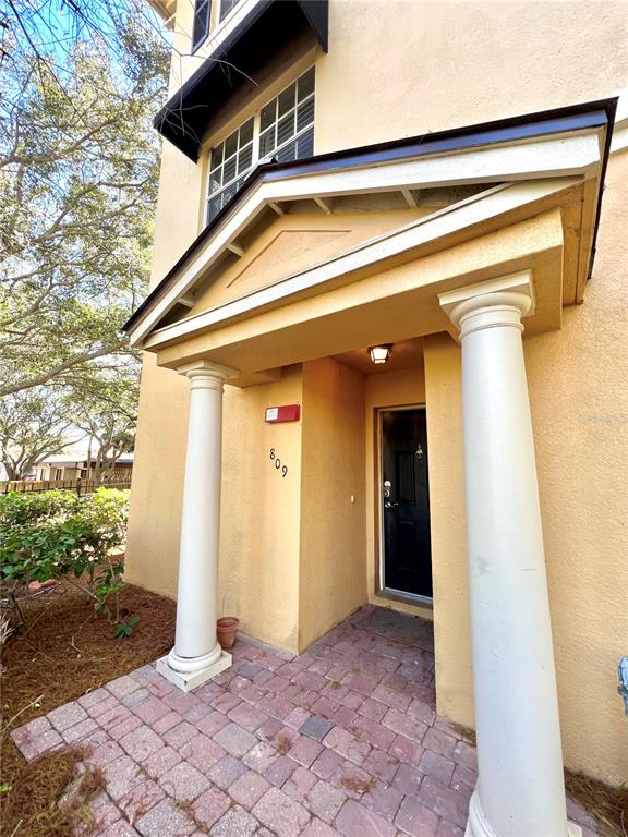 A tan building exterior features a covered entryway with two white columns and a brick patio — 809 HARBOR OAK LANE, CLEARWATER, FL