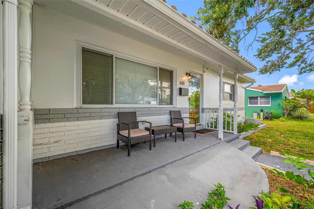 A covered front porch features a concrete floor, two wicker chairs, and a small table — 6219 HAMPTON DRIVE N, ST PETERSBURG, FL