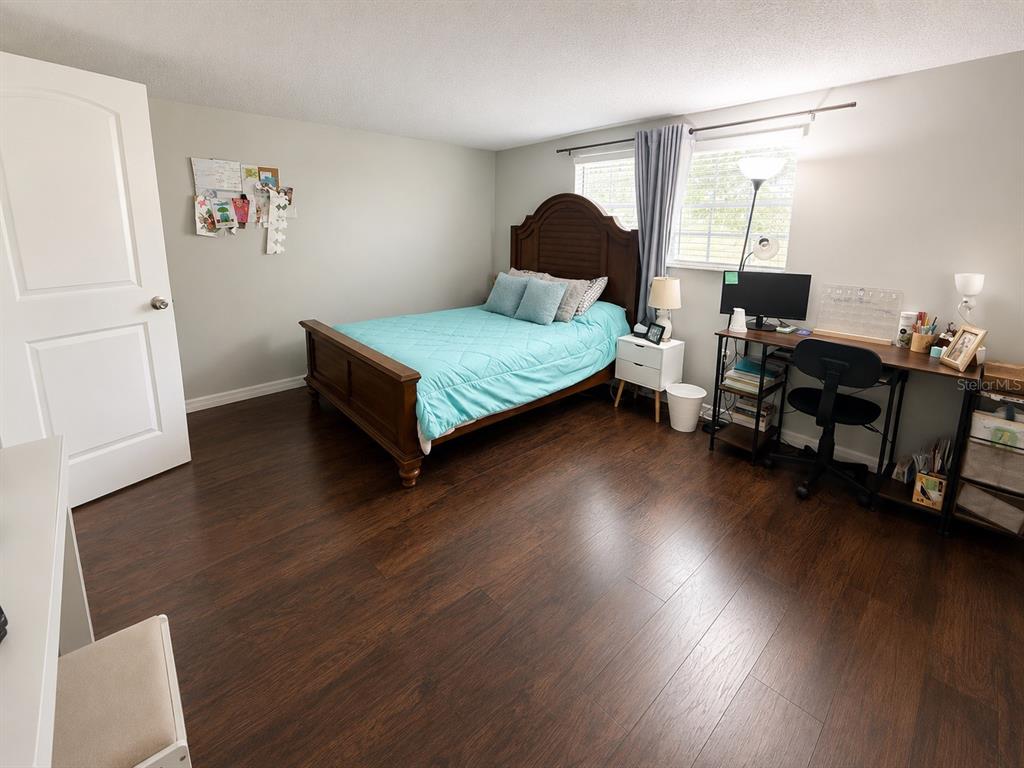 A bedroom features dark wood flooring, a bed with a teal quilt, and a desk area — 12623 CLOCK TOWER PKWY, HUDSON, FL
