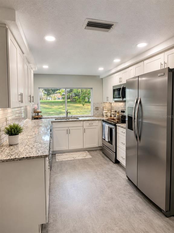 A kitchen features white cabinets, granite countertops, stainless steel appliances, and a window overlooking greenery — 12623 CLOCK TOWER PKWY, HUDSON, FL