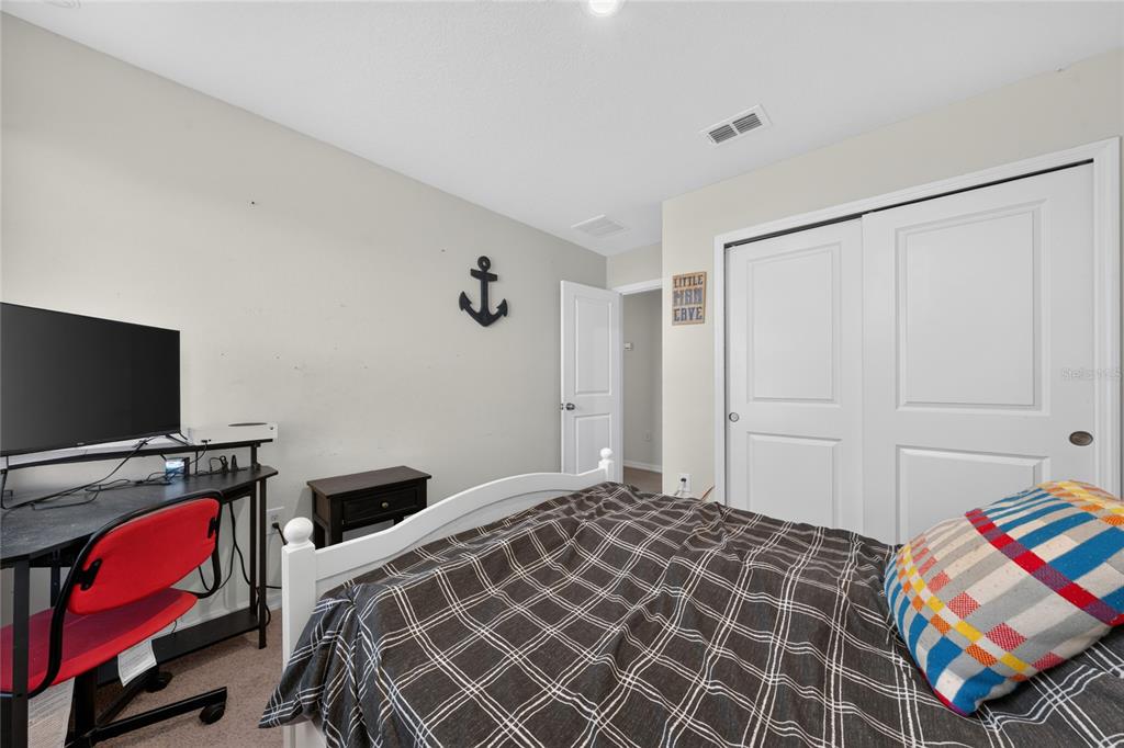 A bedroom features a white bed frame, a desk with a red chair, and closet doors — 370 QUARRY ROCK CIRCLE, KISSIMMEE, FL