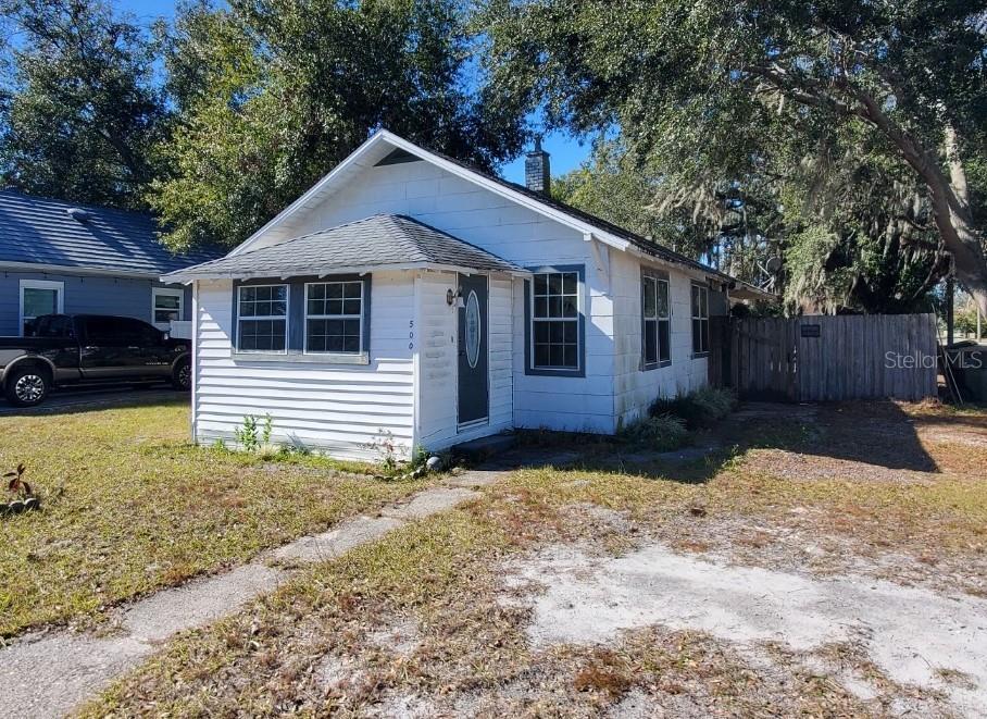 A small, white, single-story house with a front porch and a gray shingled roof — 500 MASSACHUSETTS AVENUE, ST CLOUD, FL