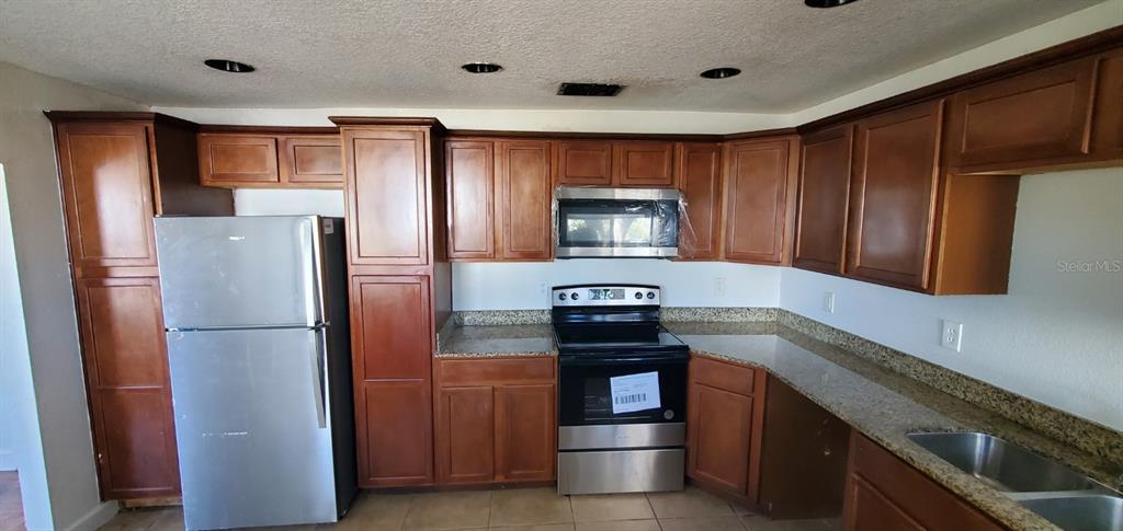 A kitchen features wood cabinets, granite countertops, stainless steel appliances, and recessed lighting — 500 MASSACHUSETTS AVENUE, ST CLOUD, FL