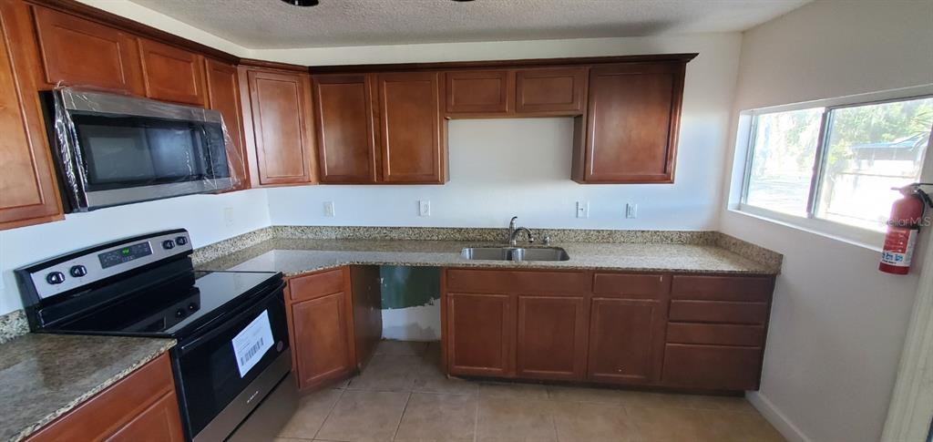 A kitchen features wood cabinets, granite countertops, a stainless steel microwave, and a black stove — 500 MASSACHUSETTS AVENUE, ST CLOUD, FL