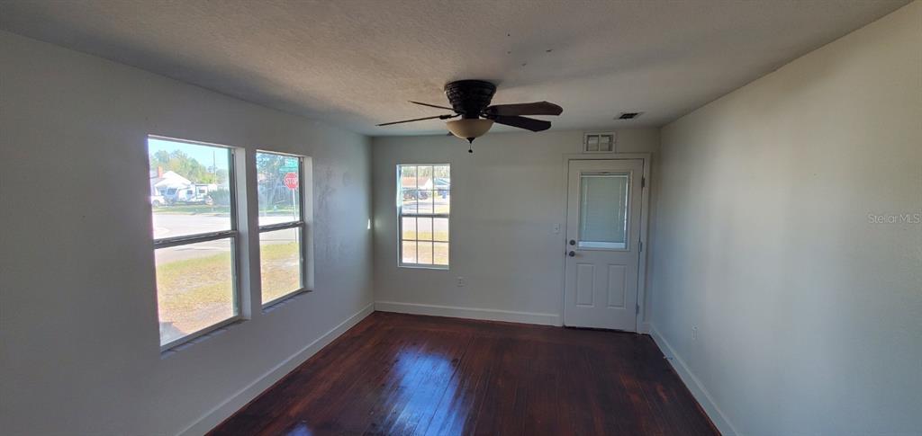 An empty room features hardwood floors, a ceiling fan, three windows, and a white door — 500 MASSACHUSETTS AVENUE, ST CLOUD, FL