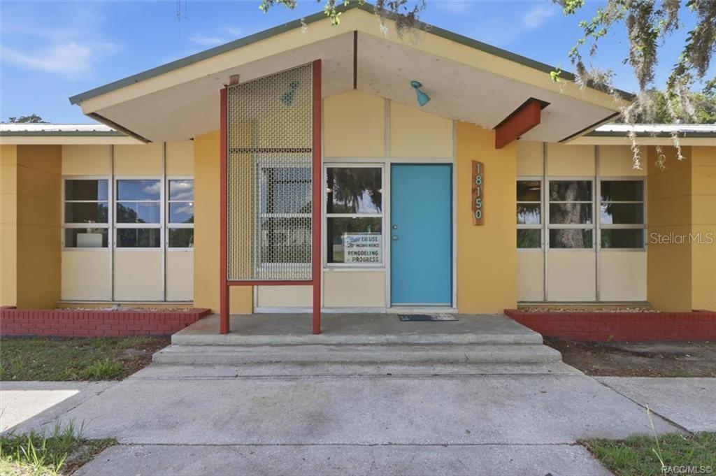 The exterior of a single-story building features yellow walls, a blue door, and red brick — 18150 SE HIGHWAY 19, INGLIS, FL