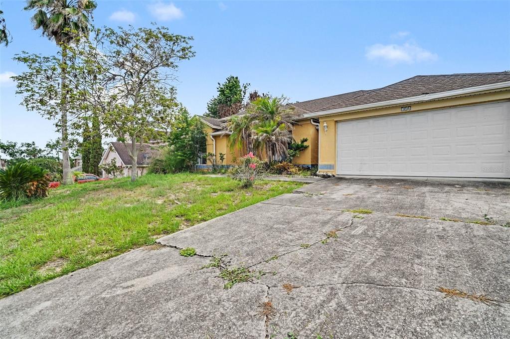 A yellow house with a two-car garage and a cracked concrete driveway — 4716 SPANIEL STREET, ORLANDO, FL