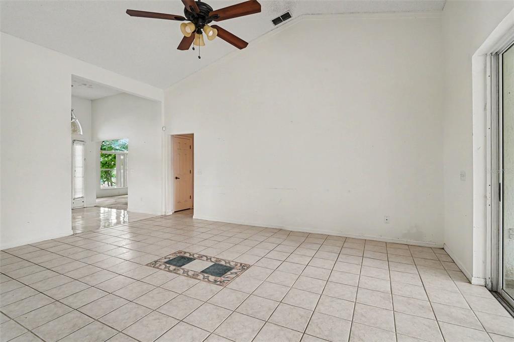 An empty living room features white walls, a vaulted ceiling, a ceiling fan, and tile flooring — 4716 SPANIEL STREET, ORLANDO, FL