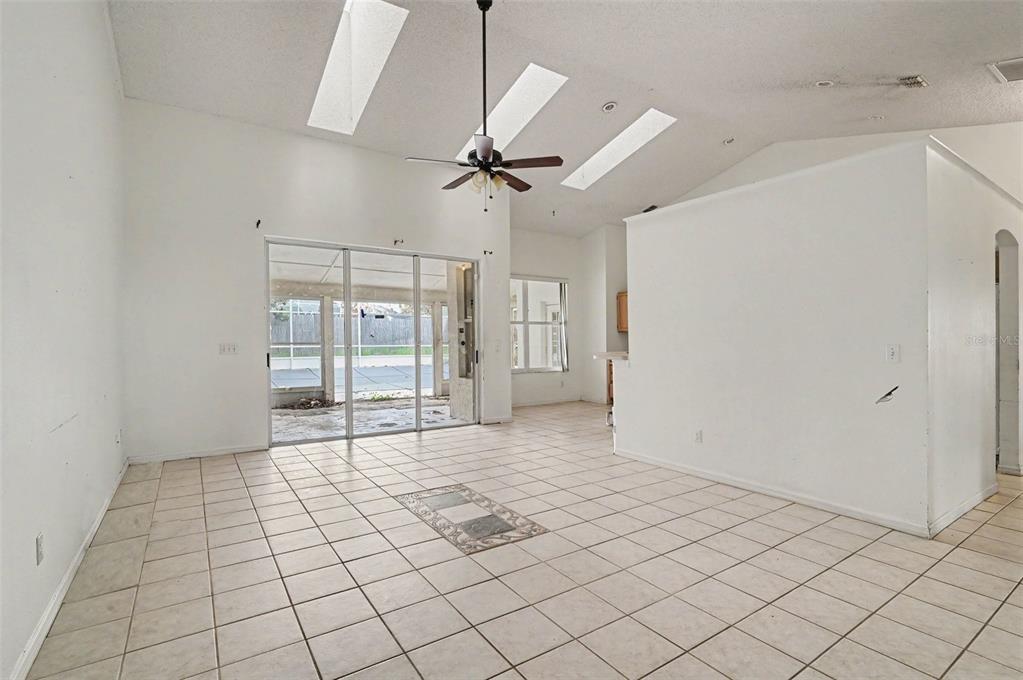 A spacious living room with white tile floors, vaulted ceilings, skylights, and sliding glass doors — 4716 SPANIEL STREET, ORLANDO, FL