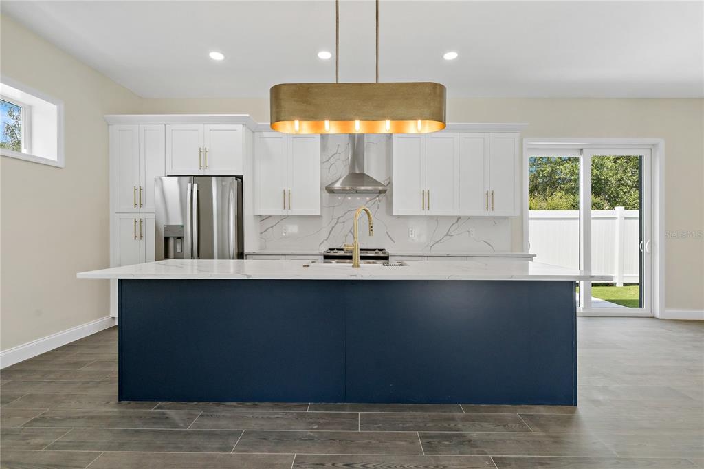 A kitchen features a navy blue island, white cabinets, marble-look backsplash, and a gold pendant light — 1348 SAN CHRISTOPHER DRIVE UNIT 2, DUNEDIN, FL
