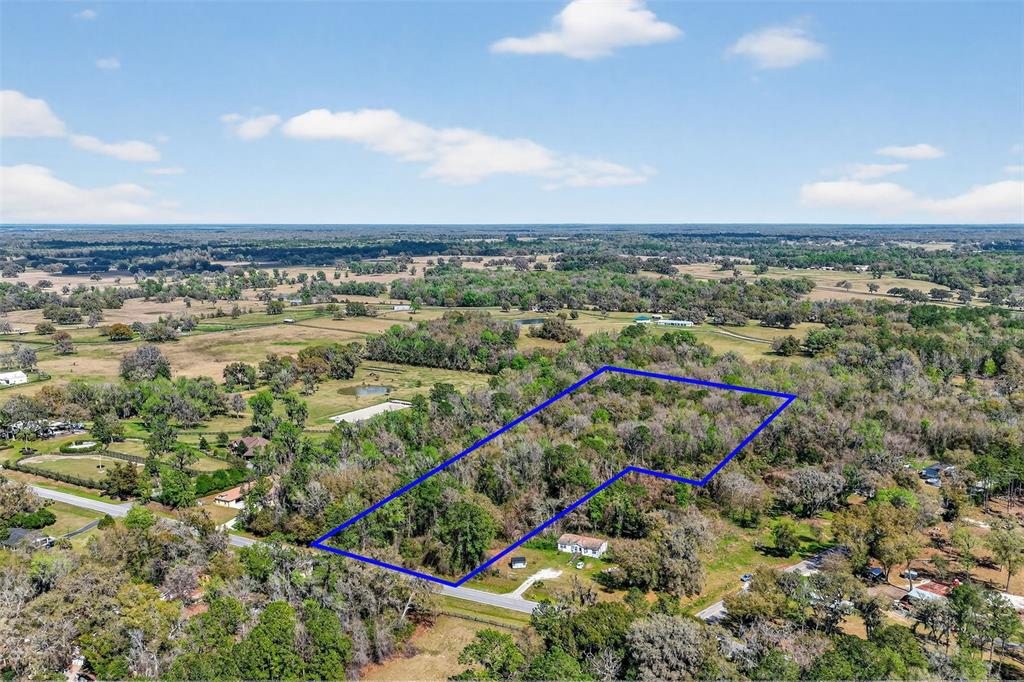 An aerial view shows a wooded lot outlined in blue with a house nearby — TBD NW HWY 225A, REDDICK, FL