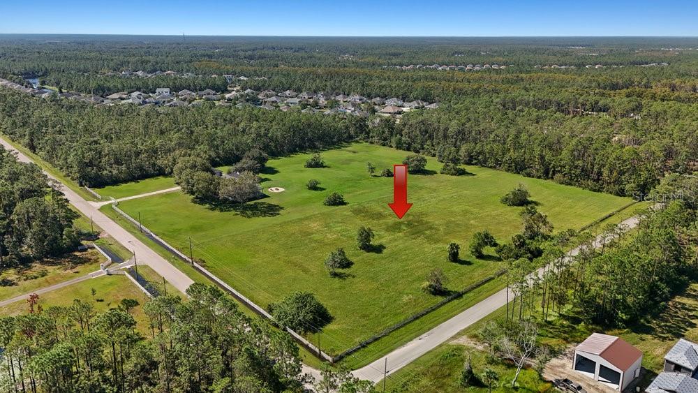 An aerial view shows a large, grassy, fenced-in plot of land surrounded by trees — 420 LEEWAY TRAIL, ORMOND BEACH, FL
