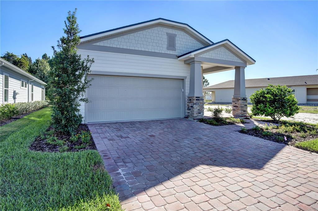 A single-story house exterior features a two-car garage, stone-based columns, and a paved driveway — 121 BEES KNEES WAY, ST AUGUSTINE, FL