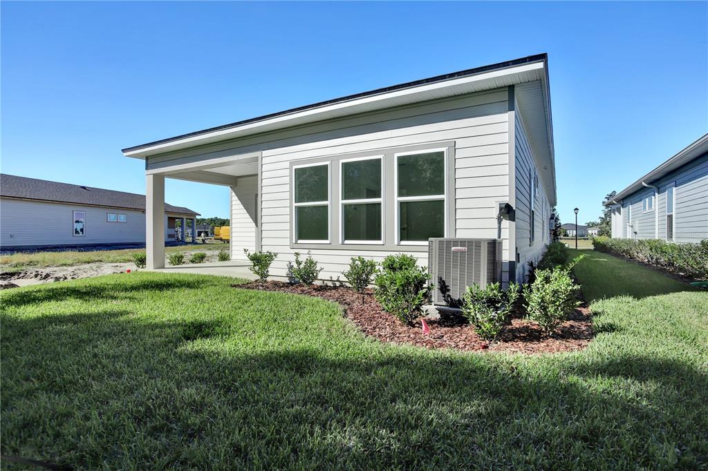 The exterior of a single-story house features light-colored siding, a covered patio, and landscaping — 121 BEES KNEES WAY, ST AUGUSTINE, FL