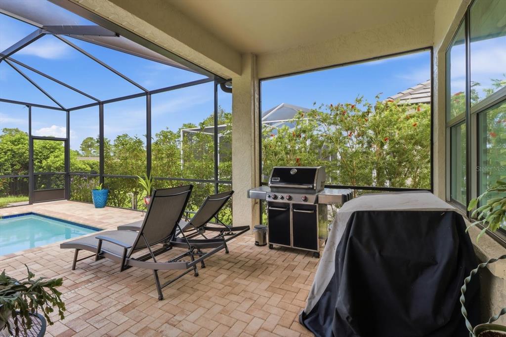 A screened-in patio features a brick paver floor, a grill, and lounge chairs by a pool — 1800 N ROSE HUE PATH, HERNANDO, FL