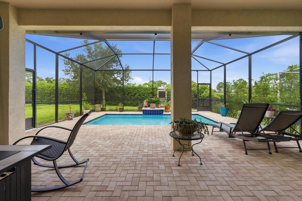 A covered patio with brick pavers overlooks a screened-in swimming pool and backyard — 1800 N ROSE HUE PATH, HERNANDO, FL