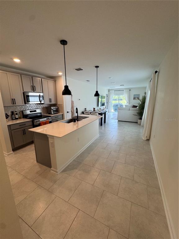 A kitchen with a central island and light-colored tile flooring opens into a living area — 2127 GREEN VALLEY STREET, DAYTONA BEACH, FL