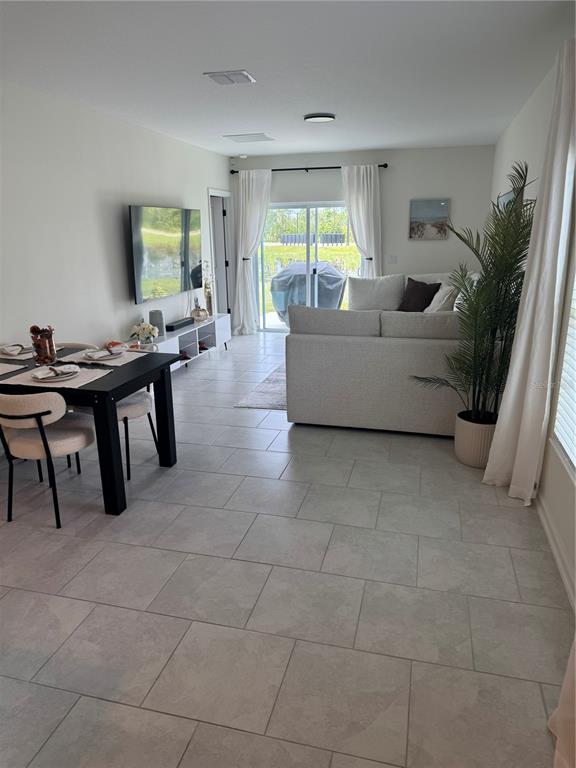 An open-concept living and dining area features light tile flooring, a sectional sofa, and sliding doors — 2127 GREEN VALLEY STREET, DAYTONA BEACH, FL