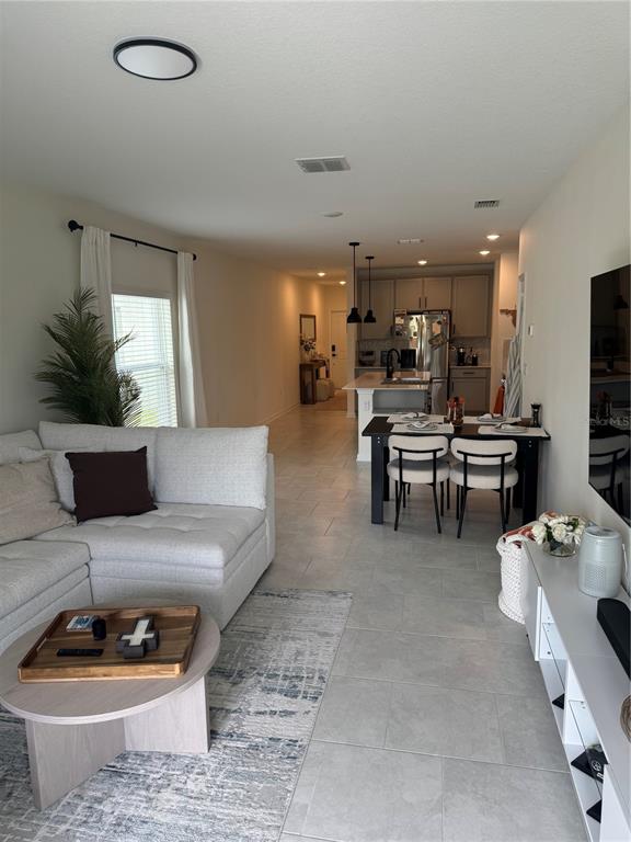 An open-concept living room and kitchen feature light tile flooring and neutral furniture — 2127 GREEN VALLEY STREET, DAYTONA BEACH, FL