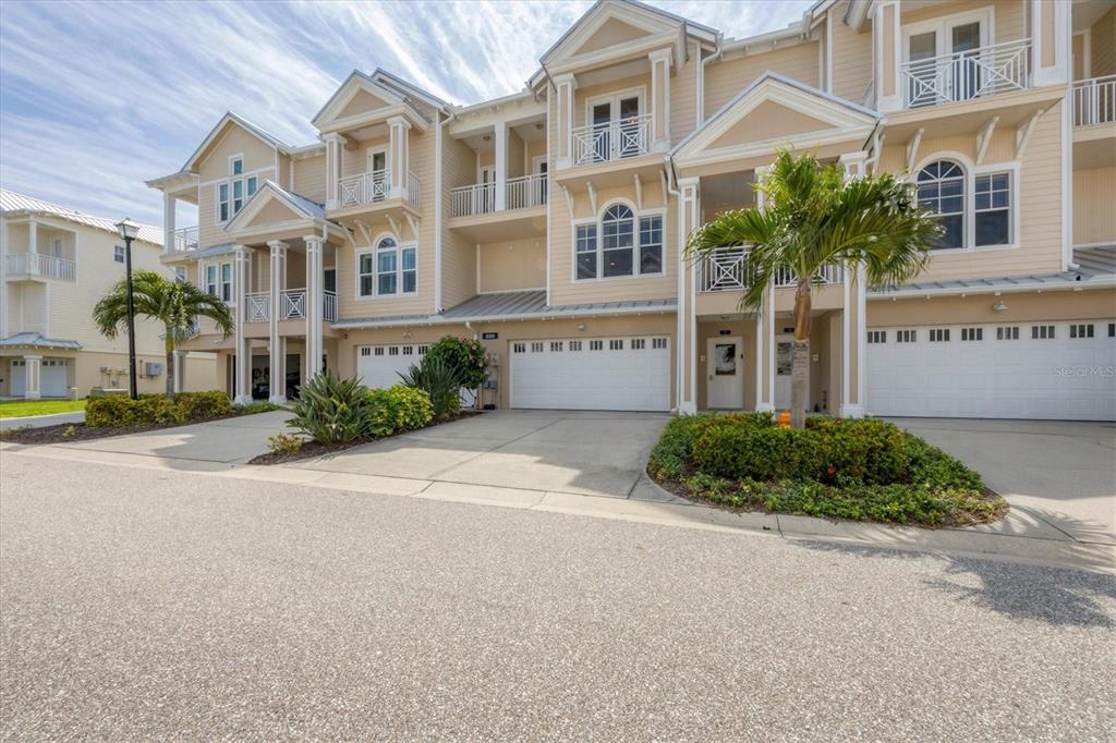 A row of three-story townhouses with beige siding, white trim, and attached garages — 10380 LONGSHORE ROAD UNIT 77, PLACIDA, FL