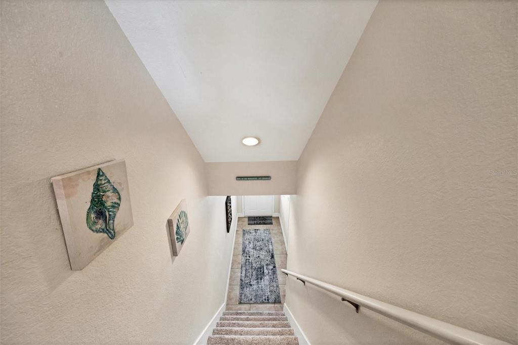 A carpeted staircase leads down to a tiled entryway with a runner rug — 10380 LONGSHORE ROAD UNIT 77, PLACIDA, FL