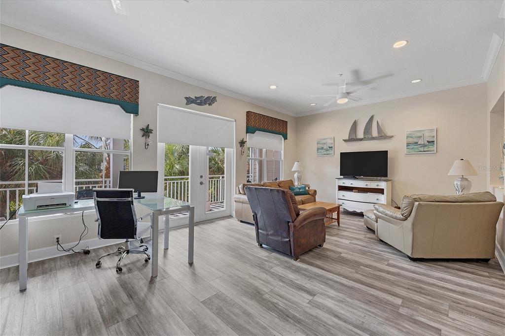 A living room with a home office area, light wood-look flooring, and a balcony view — 10380 LONGSHORE ROAD UNIT 77, PLACIDA, FL