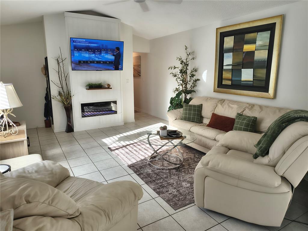 A living room features a wall-mounted television above an electric fireplace, tile flooring, and furniture — 255 BOUNDARY BOULEVARD UNIT 104, ROTONDA WEST, FL