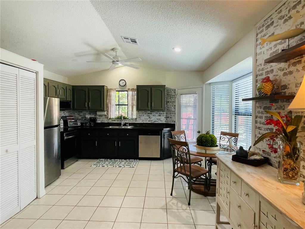 A kitchen features dark green upper cabinets, black lower cabinets, stainless steel appliances, and tile flooring — 255 BOUNDARY BOULEVARD UNIT 104, ROTONDA WEST, FL