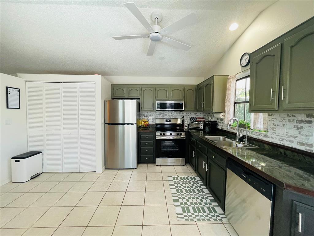 A kitchen features olive green cabinets, stainless steel appliances, and light-colored tile flooring — 255 BOUNDARY BOULEVARD UNIT 104, ROTONDA WEST, FL