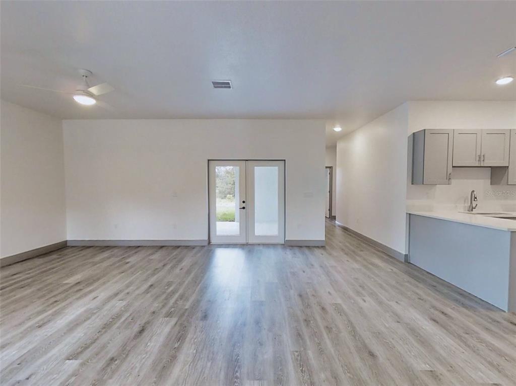 A bright, open-concept living area features light wood-look flooring, white walls, and glass patio doors — 2 GUAVA LANE, OCKLAWAHA, FL