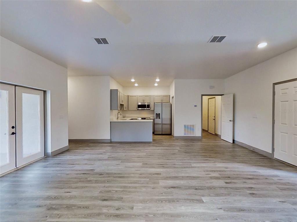 An open-concept living area features light wood-look flooring, white walls, and a small kitchen — 2 GUAVA LANE, OCKLAWAHA, FL