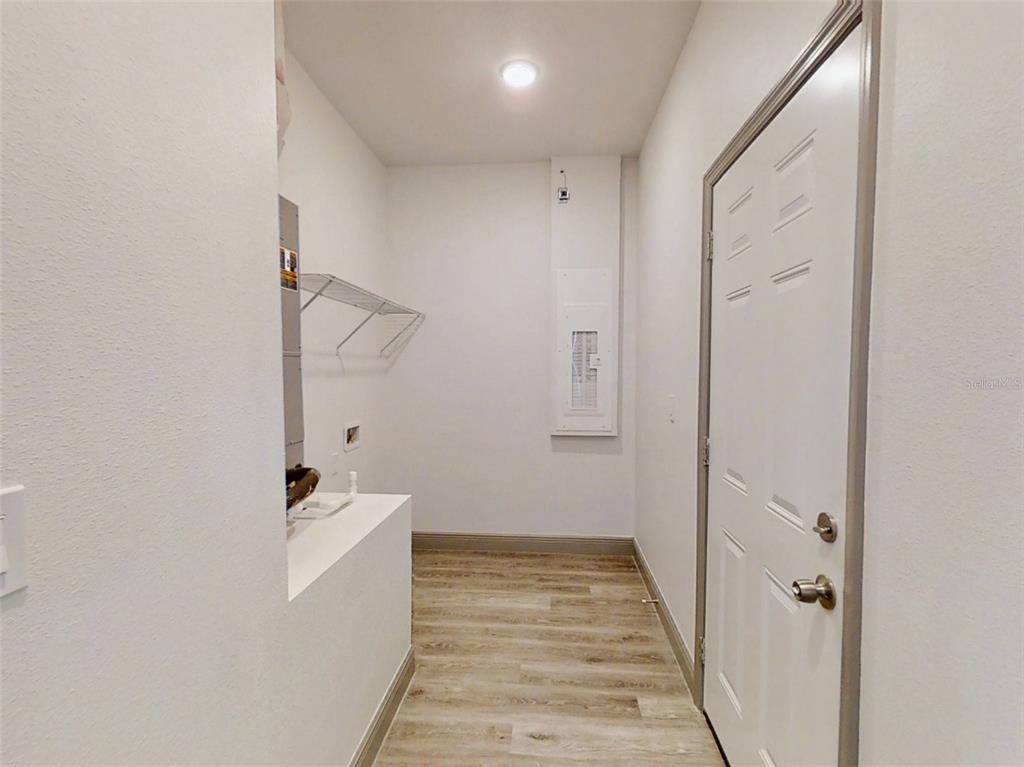 A laundry room features light wood-look flooring, a white door, and a wall-mounted electrical panel — 2 GUAVA LANE, OCKLAWAHA, FL